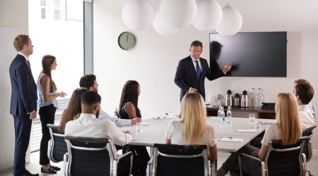 Mature Businessman Addressing Group Meeting Around Table At Graduate Recruitment Assessment Day