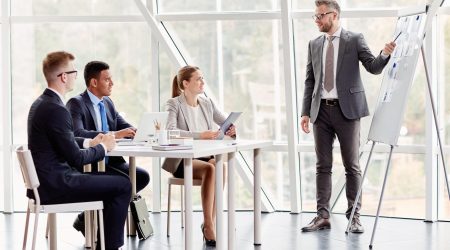 Group of young managers looking at businessman pointing at paper with data on whiteboard